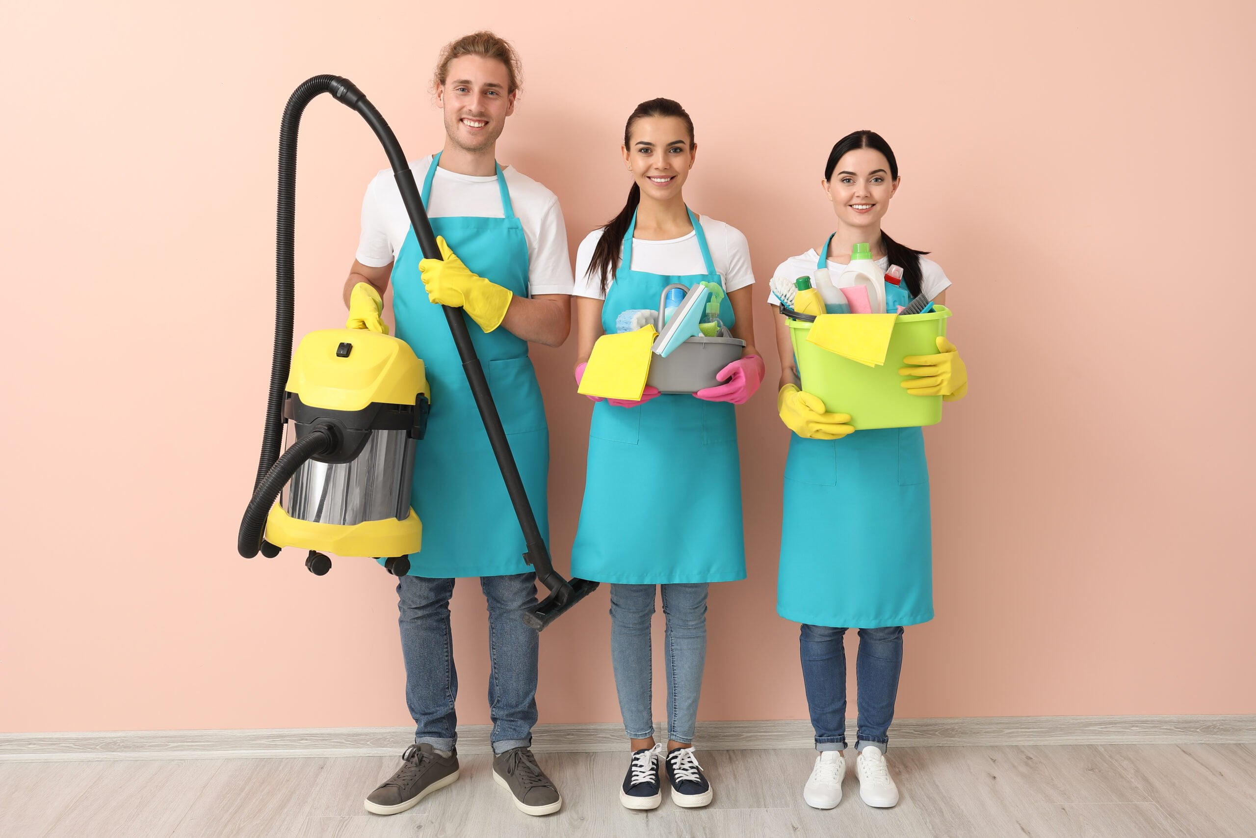 man and women together wearing a complete uniform holding their cleaning materials with pink wall at the background