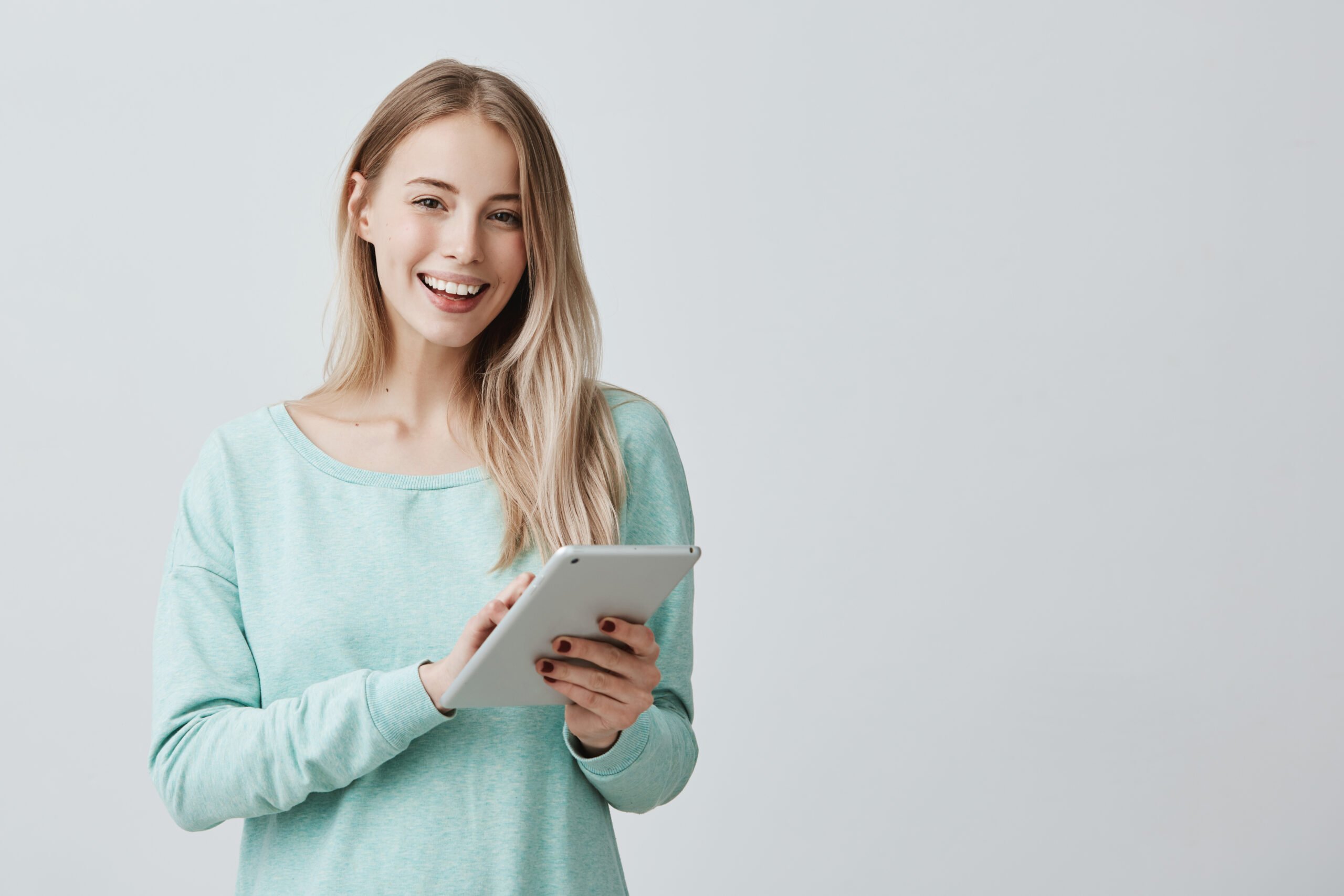 a happy woman wearing a light blue long sleeve holding a tablet device